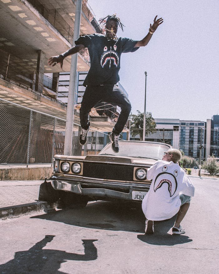 journey Man jumps in urban setting showcasing streetwear fashion with vintage car.
