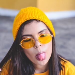 A young woman in stylish yellow attire sticks out her tongue in a playful gesture outdoors.